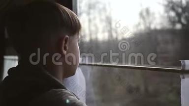 这个男孩站在火车窗口，看着窗外的风景。 坐火车旅行。 旅游业