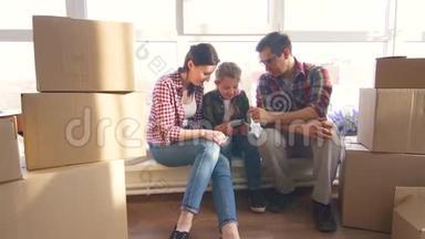 幸福的年轻夫妇和女儿坐在窗台上享受智能手机