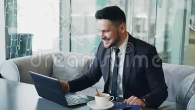 穿着正式服装的白人商人通过笔记本电脑网络摄像头聊天，在一家高档咖啡馆里愉快地挥动着他的手