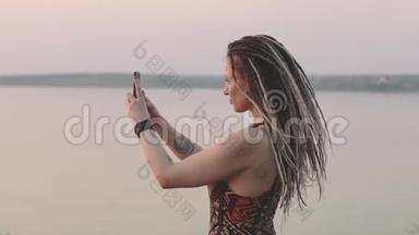 迷人的嬉皮士女人，带着可怕的家伙，在<strong>海边</strong>日落时用智能手机<strong>拍照</strong>