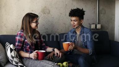 年轻的白种人<strong>女孩</strong>和英俊的穆拉特都穿着城市服装，坐在沙发上<strong>喝茶</strong>，说话。