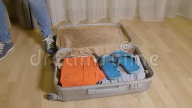 女人把东西和衣服放在旅行箱里，放在家里的地板上