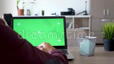 在笔记本电脑上工作的人的后拍，上面有绿色屏幕