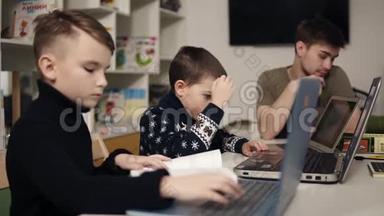 两个小男孩在笔记本电脑键盘上打字，而他们的男程序员老师正坐在附近。