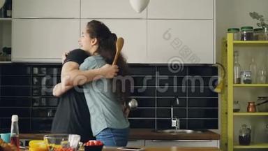快乐的一对夫妇在厨房里用大勺子击剑，在家做早餐时互相拥抱