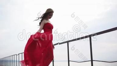 一位穿着红色长裙的美女站在海上码头，风很大