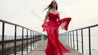 无忧无虑的微笑的女人走过码头，挥舞着她的丝红色连衣裙