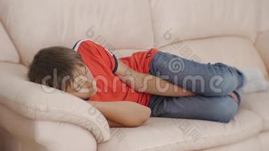年轻人睡在沙发上。 白天穿红色t恤和蓝色牛仔裤睡在米色皮革沙发上的白人少年