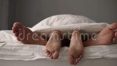 一对年轻美丽可爱的夫妇躺在床上。 他们的脚在毯子下，而早上在床上醒来