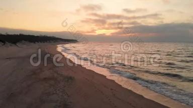 空中观看无人机镜头低飞行在一个废弃的海滩上日落。 带着滚滚海浪和夕阳的沙岸