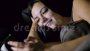 女孩晚上躺在卧室的床上上网，看照片，聊天和微笑。
