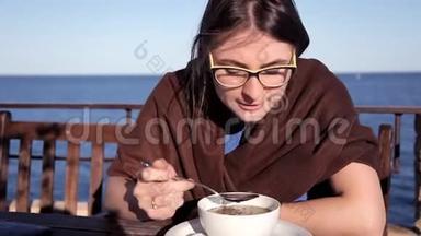 傍晚日落时分，一个女孩坐在一家俯瞰大海的咖啡馆里，铺着毯子，吃<strong>热汤</strong>