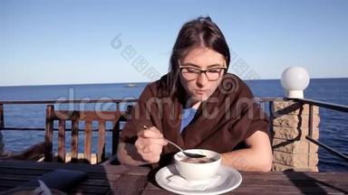 傍晚日落时分，一个女孩坐在一家俯瞰大海的咖啡馆里，铺着毯子，吃热汤