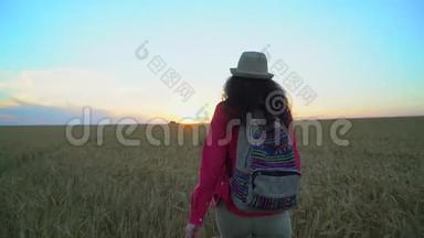 <strong>夏日</strong>夕阳下，女游客漫步麦田。 徒步旅行者女人戴着<strong>帽子</strong>，背着背包徒步旅行。 女孩
