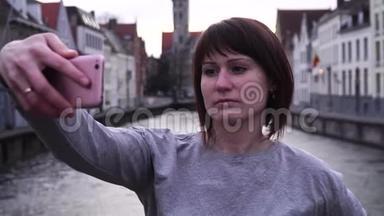 女孩游客在比利时布鲁日日落时在智能手机上自拍。 慢动作