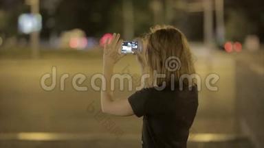 美丽的年轻女子在夜街拍智能手机