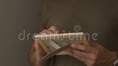 一个孤独的人站在窗前，拿着一张木框里的照片。 人检查照片..