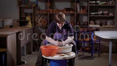 一个成年女人正在创作一个<strong>陶土</strong>花瓶，她坐在陶工`轮子后面，形成一篇<strong>陶土</strong>文章