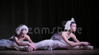 在聚光灯下，在老剧院大厅的舞台上。 年轻的芭蕾舞演员穿着白色天鹅和尖角鞋
