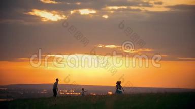 年轻的女人和她的丈夫在田里玩飞盘，站在他们的小儿子旁边，日落的夏天晚上-