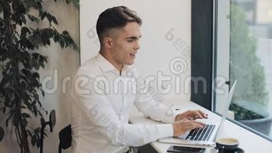 快乐的年轻商人在窗户附近的咖啡馆里用笔记本电脑工作。 商业，事业，成功，自由职业者，求职