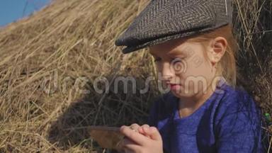 年轻可爱的女孩带着帽子玩得很开心，坐在<strong>干草</strong>堆里用电话。 坐在<strong>干草上</strong>的小女孩。