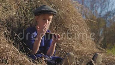 年轻可爱的女孩带着帽子玩得很开心，坐在<strong>干草</strong>堆里用电话。 坐在<strong>干草上</strong>的小女孩。