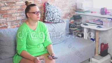 年轻无聊的女人坐在家里的沙发上看<strong>电视</strong>。 4k
