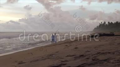 恋爱中的年轻夫妇在日落时分在海滩上<strong>散步</strong>，<strong>手牵手</strong>