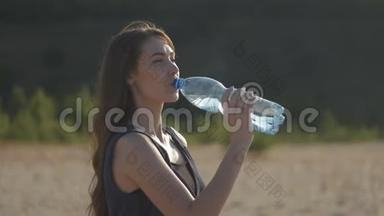 小可爱的女人在炎热的夏天从大自然中的塑料瓶里喝水。 女孩渴望喝水