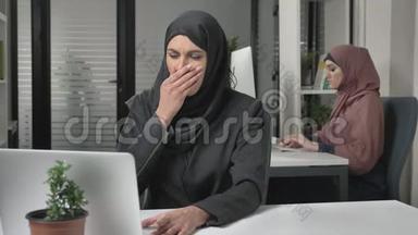 戴黑色头巾的女孩坐在办公室里咳嗽，一种疾病，一种感冒，一种疾病是一个概念。穿粉色头巾的女孩