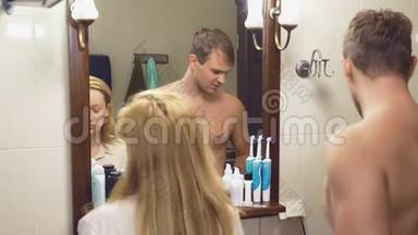 美丽的夫妻，男人和女人，一起在镜子前的浴室里洗。 4K，动作慢，一个男人在刮胡子