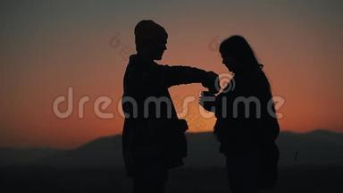 在美丽的夕阳背景下，一对相爱的年轻夫妇用<strong>热水</strong>瓶<strong>喝</strong>茶的剪影