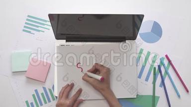 女人在笔记本电脑<strong>上</strong>的<strong>一张</strong>纸<strong>上</strong>写SEMINA R。 带有图表的办公桌面。
