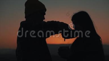 在美丽的夕阳背景下，一对相爱的年轻夫妇用热水瓶喝茶的剪影