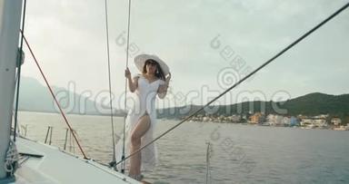 在游艇上的<strong>女士</strong>。 一个穿着白色<strong>长裙</strong>，戴着大帽子的女人站在船上，在一个多风的天气里骑过湖面