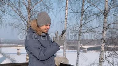 穿着蓝色<strong>羽绒服</strong>，带皮帽的人在冬季公园里用手机视频聊天。
