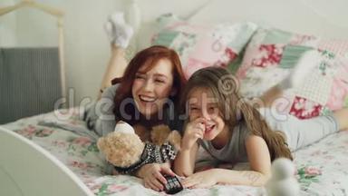 早上躺在家里的时候，开心的妈妈和可爱的女儿在电视上看有趣的卡通电影