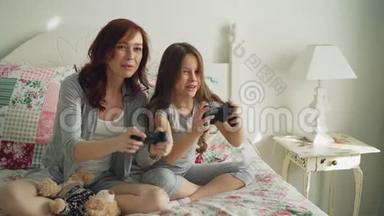 有趣的笑女孩和快乐的年轻妈妈在电视上玩电脑控制台游戏时玩得很开心坐在家里