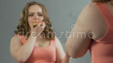 年轻的女士在镜子里<strong>鄙视</strong>自己超重的身体，同时吃甜甜圈