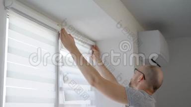成年男子白天在客厅的窗框上安装百叶窗杆并固定窗帘