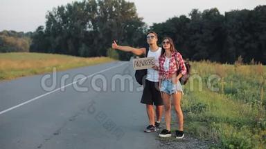 一对年轻夫妇正站在路上搭便车。 一男一女在高速公路上停着一个牌子