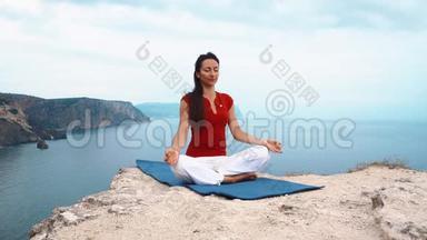 女孩坐在海边的岩石上，冥想莲花瑜伽姿势，集中注意力，放松心灵，灵魂和身体。