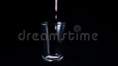 草莓奶昔分离在黑色背景上。 在透明玻璃中，在黑色背景上倒入粘稠的粉红色奶昔