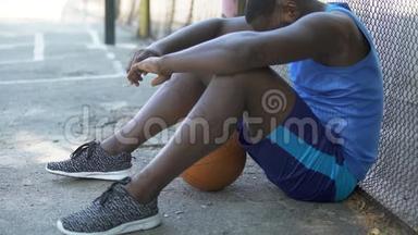 悲伤的非裔美国篮球运动员坐在地上，缺乏动力
