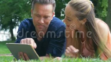 一对夫妇在公园里不寒而栗，在他们的平板电脑上看照片，并在社交网络上发布