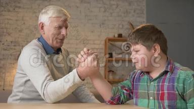 祖父和孙子在家里舒适的房间里<strong>摔跤</strong>。 在手臂<strong>摔跤</strong>中测量力量。 小胖孩子