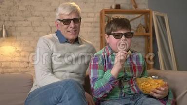 祖父和孙子坐在沙发上，戴着3D<strong>眼</strong>镜看一部3D电影，吃着薯片，笑着，笑着