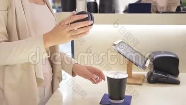 一位年轻女子在<strong>咖啡吧</strong>台买咖啡并在黑纸杯上盖上帽子的慢速特写镜头
