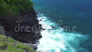 暴风雨时海浪溅落在岩石峭壁上. 蓝色的海浪随着泡沫和浪花破碎到石质海岸。 绿松石